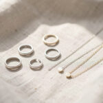 Sélection élégante de bijoux minimalistes posés sur un tissu clair, éclairage doux et ambiance apaisante, détails métalliques délicats et composition harmonieuse.
