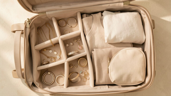 Organisateur de bijoux soigneusement rangé dans une petite valise cabine ouverte, avec colliers, bagues, bracelets et boucles d’oreilles séparés dans des compartiments souples.
